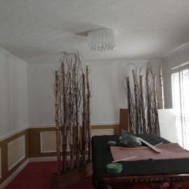 Two large decorative branch structures in wooden bases stand on a red carpet in a room with a central chandelier.