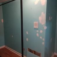 A teal wall with several white spackle patches and a square vent cover, showing signs of home repair in a room.