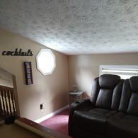 A cozy lounge with pink carpet, a dark brown leather recliner, a small side table, and wall decor reading 