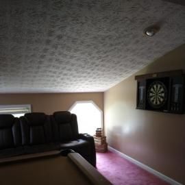 A room with a dartboard on a tan wall, dark leather recliners, a pool table in the foreground, and pink carpet.
