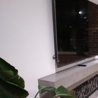 A flat-screen television mounted above a minimalist concrete fireplace with decorative metal details, next to a plant.