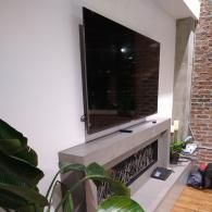A large flat-screen TV mounted on a light gray, modern fireplace mantle with an exposed brick wall to the right.