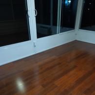 A corner of a room featuring dark polished hardwood floors meeting white-framed sliding glass doors at night.