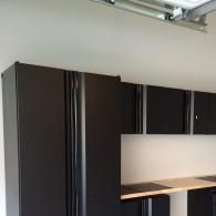 Dark cabinets with vertical handles and a light-colored countertop mounted on a white wall in a garage.