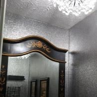 An ornate dark wooden mirror frame with gold floral details mounted on a wall with silver glitter wallpaper.