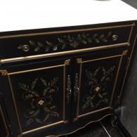 A black wooden cabinet featuring gold hand-painted floral motifs, gold trim, and two central doors with silver pulls.