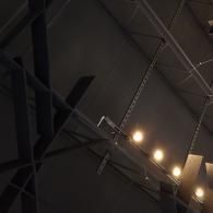 Low-angle view of dark, angular ceiling beams and architectural lighting structures in an industrial-style interior.