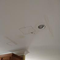 A white ceiling with water stains, two square access panels, and a recessed ceiling light.