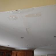 A white ceiling with water damage, showing bubbling paint and stains near the top edge and around recessed lights.