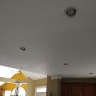 Low-angle view of a white ceiling with four recessed circular lights, showing a glimpse of a yellow kitchen area below.