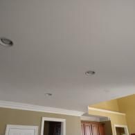A room ceiling with three recessed lights, crown molding, and partial views of tan walls and a wooden cabinet.