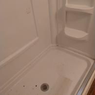 A clean, white fiberglass shower stall interior featuring a built-in shelf unit and a central floor drain.