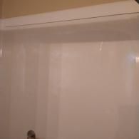 A white, high-gloss shower surround with a top ledge and a portion of a chrome fixture visible at the bottom.