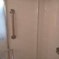 A stainless steel grab bar mounted vertically on a plain white shower wall.