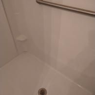 A white walk-in shower stall with a built-in soap shelf and a horizontal grab bar installed on the wall.