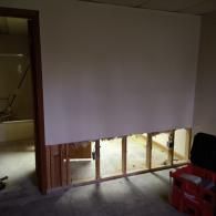 A wall with exposed wooden studs in the lower section, showing an unfinished home renovation project.