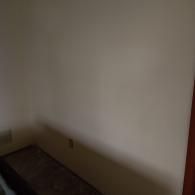 A plain, light-colored interior wall with a small electrical outlet near the bottom corner above a carpeted floor.