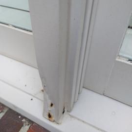 Close-up of a white painted wooden window frame corner with visible rust stains and peeling paint on the sill.