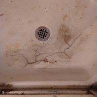 A close-up view of a dirty white shower floor with a central drain and a branching crack across the surface.