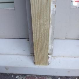 A close-up view of a vertical, light-colored wooden post installed on a gray-painted base against a gray background.