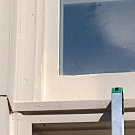 A close-up view of a beige window frame with a metal ladder leaning against the bottom sill under a blue sky.