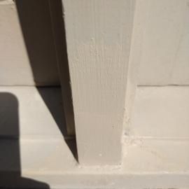 A close-up view of a vertical, light-colored wooden post meeting a horizontal beam, with a sharp shadow cast to the left.