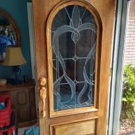 A wooden front door with a decorative arched glass panel featuring a swirling, leaf-like etched design.