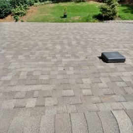 A high-angle view of a grey, rectangular brick patio leading to a patch of green grass in the background.