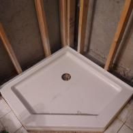 A white neo-angle shower pan installed in the corner of a room with exposed wall studs.