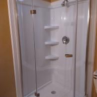 A walk-in shower with white walls, three integrated corner shelves, a silver faucet, and a clear glass folding door.