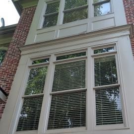 A tall, multi-pane window with beige trim set against a red brick exterior wall.