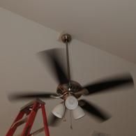 A brown ceiling fan with three lights is spinning with a red step ladder partially visible underneath it.