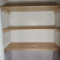 Three light-colored wooden shelves mounted inside a small, white-walled closet.