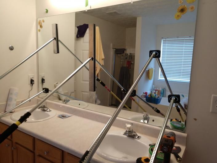 A metal frame clamp is attached to a bathroom mirror above two sinks, likely to hold the mirror securely in place.