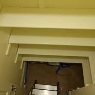 Looking down a staircase from above at a set of pale, painted wooden steps leading to a dark, unfinished basement area.