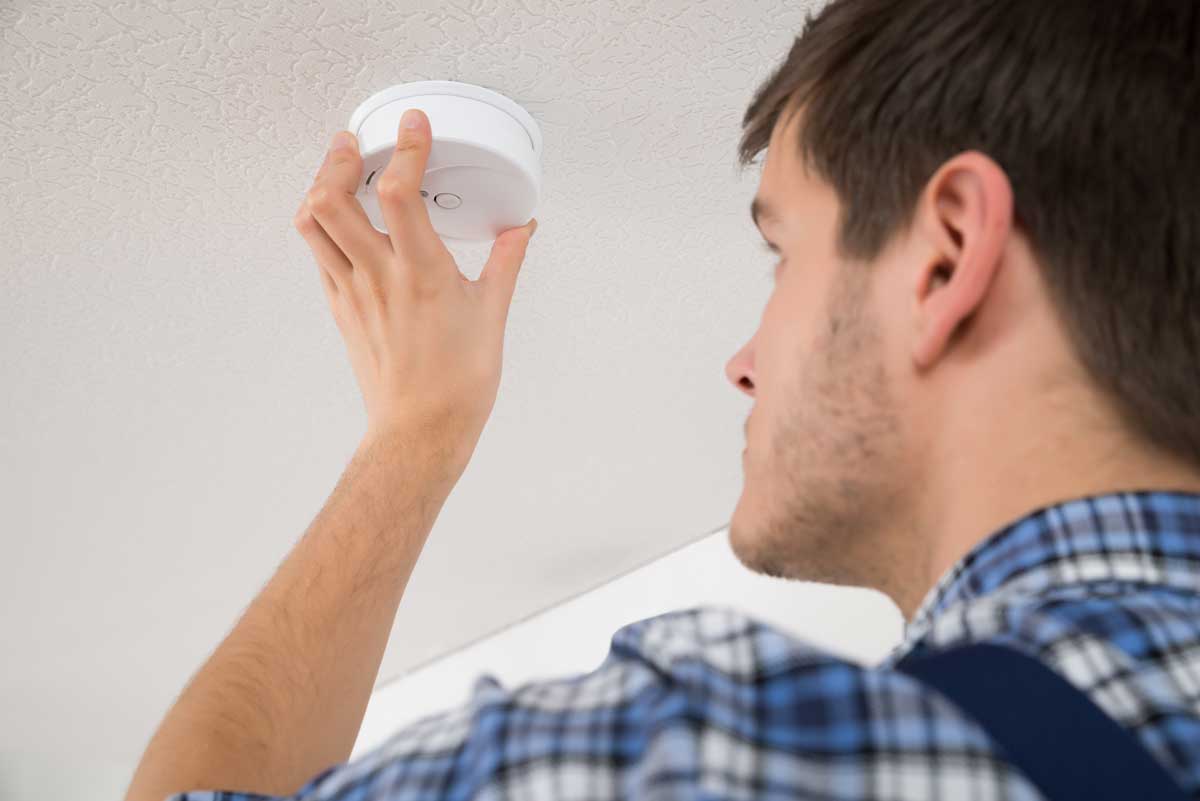 A man is installing a smoke detector on the ceiling.