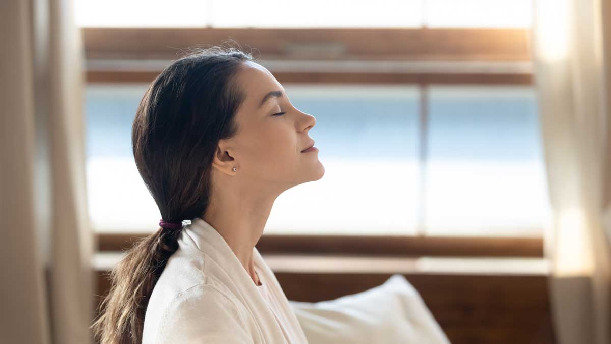 A woman is sitting in front of a window with her eyes closed.