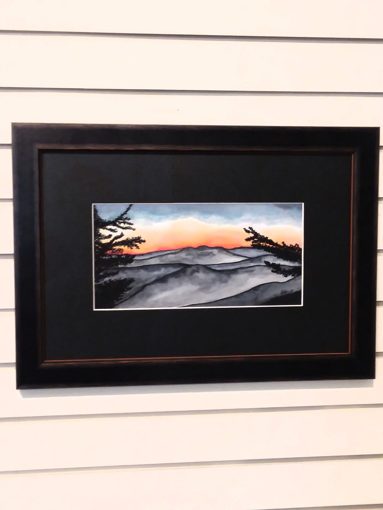 A framed painting of a sunset over a body of water