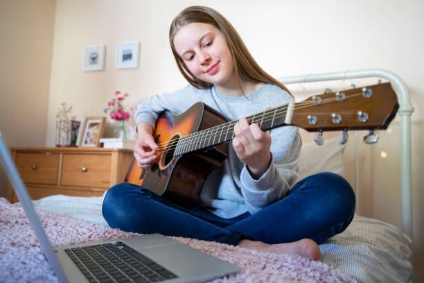 Teenage girl taking Guitar Lessons in Holly Springs, NC, learning acoustic guitar online with laptop