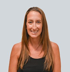 A person with long brown hair smiling against a plain, light grey background.