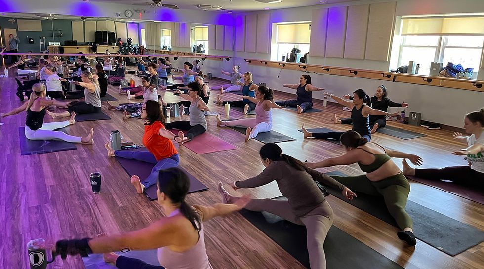 A group of people practicing yoga on mats in a studio with wooden floors and purple accent lighting.