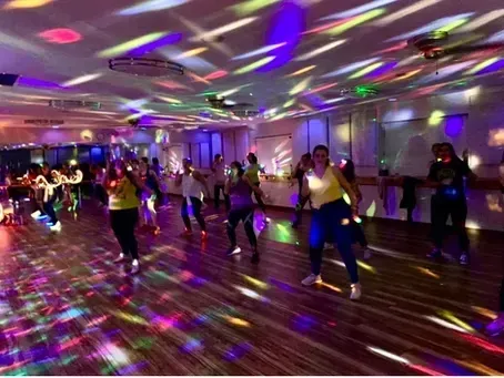 A group of people dancing in a studio illuminated by vibrant, multi-colored disco lights.
