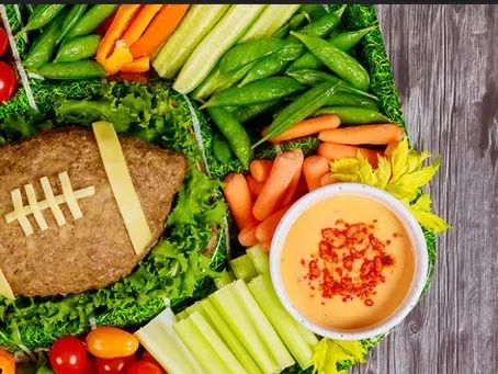A football-shaped meatloaf on a bed of lettuce, served with celery, carrots, snap peas, tomatoes, and a bowl of dip.
