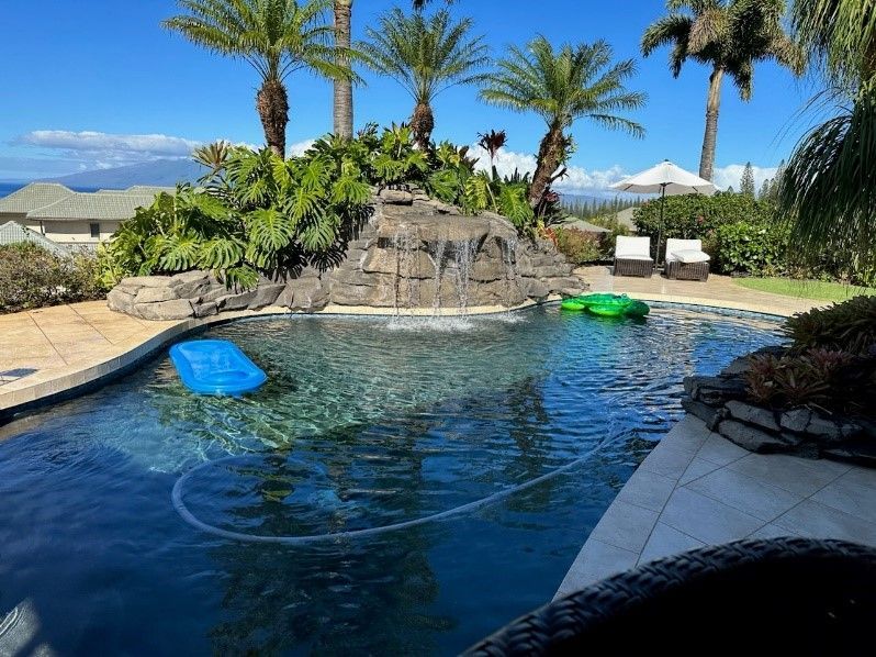 A large swimming pool with a waterfall and palm trees in the background.