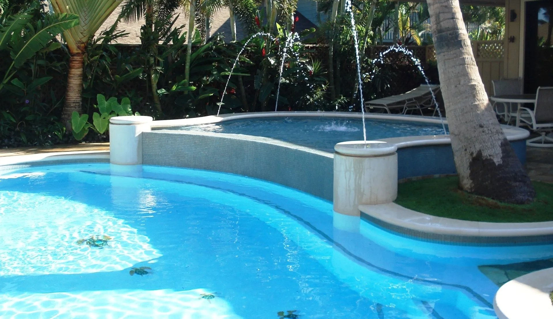 Outdoor pool with hot tub, fountains, and tropical plants.