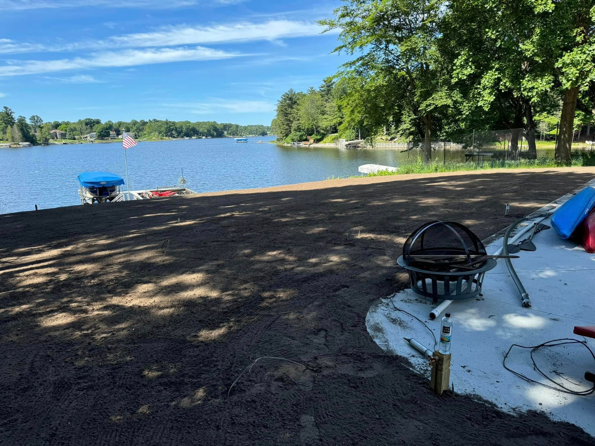 A fire pit is sitting on the beach next to a lake.