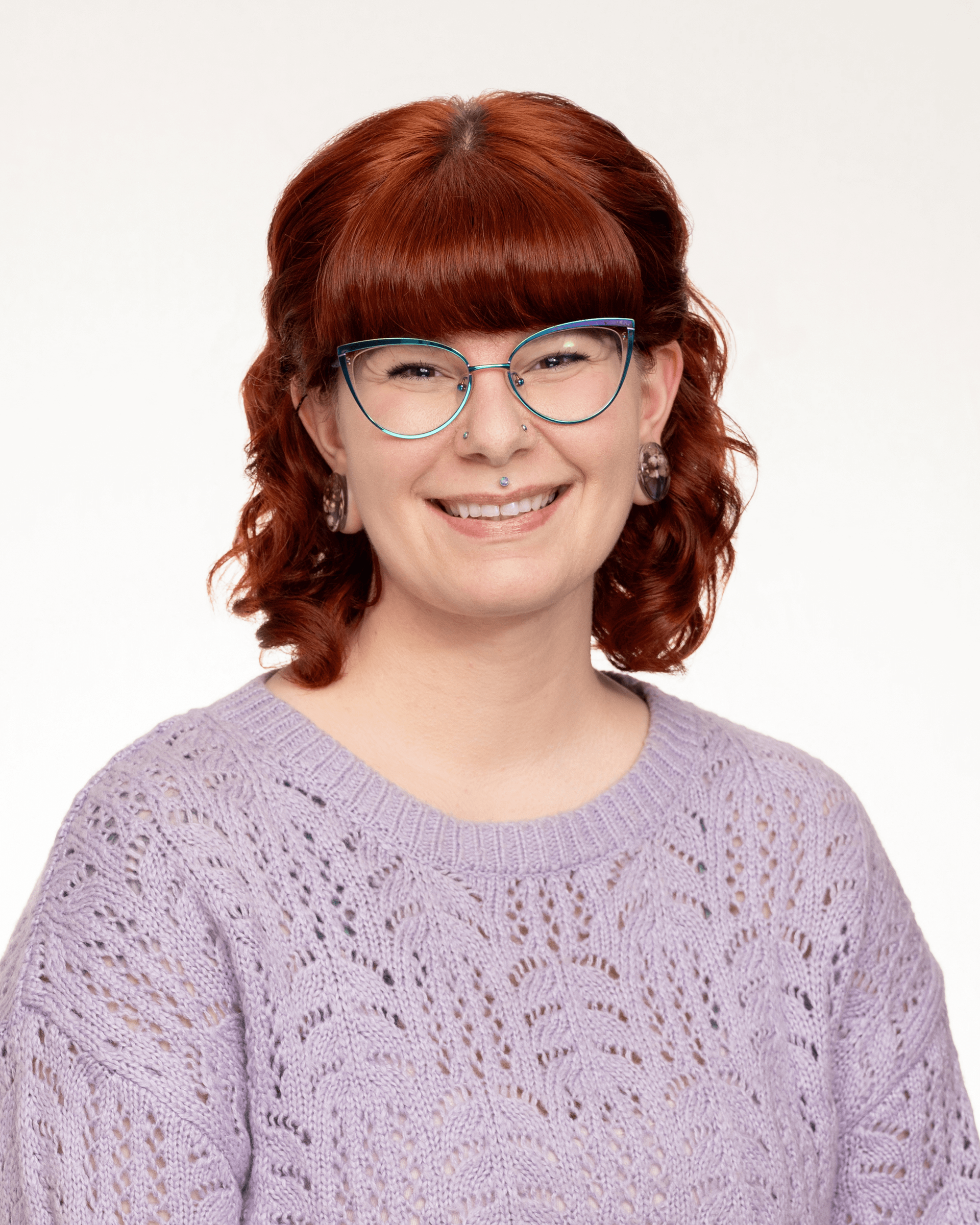 a woman with red hair and glasses is wearing a purple sweater .