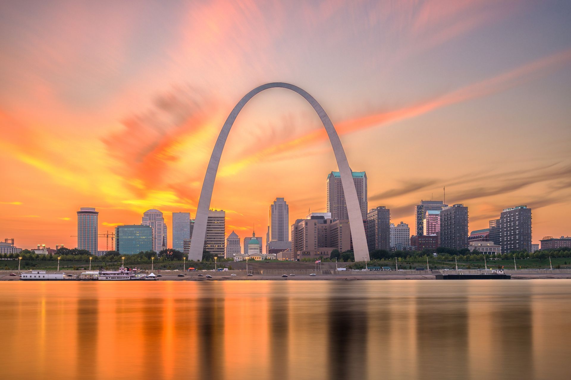 the st. louis arch is reflected in the water at sunset .