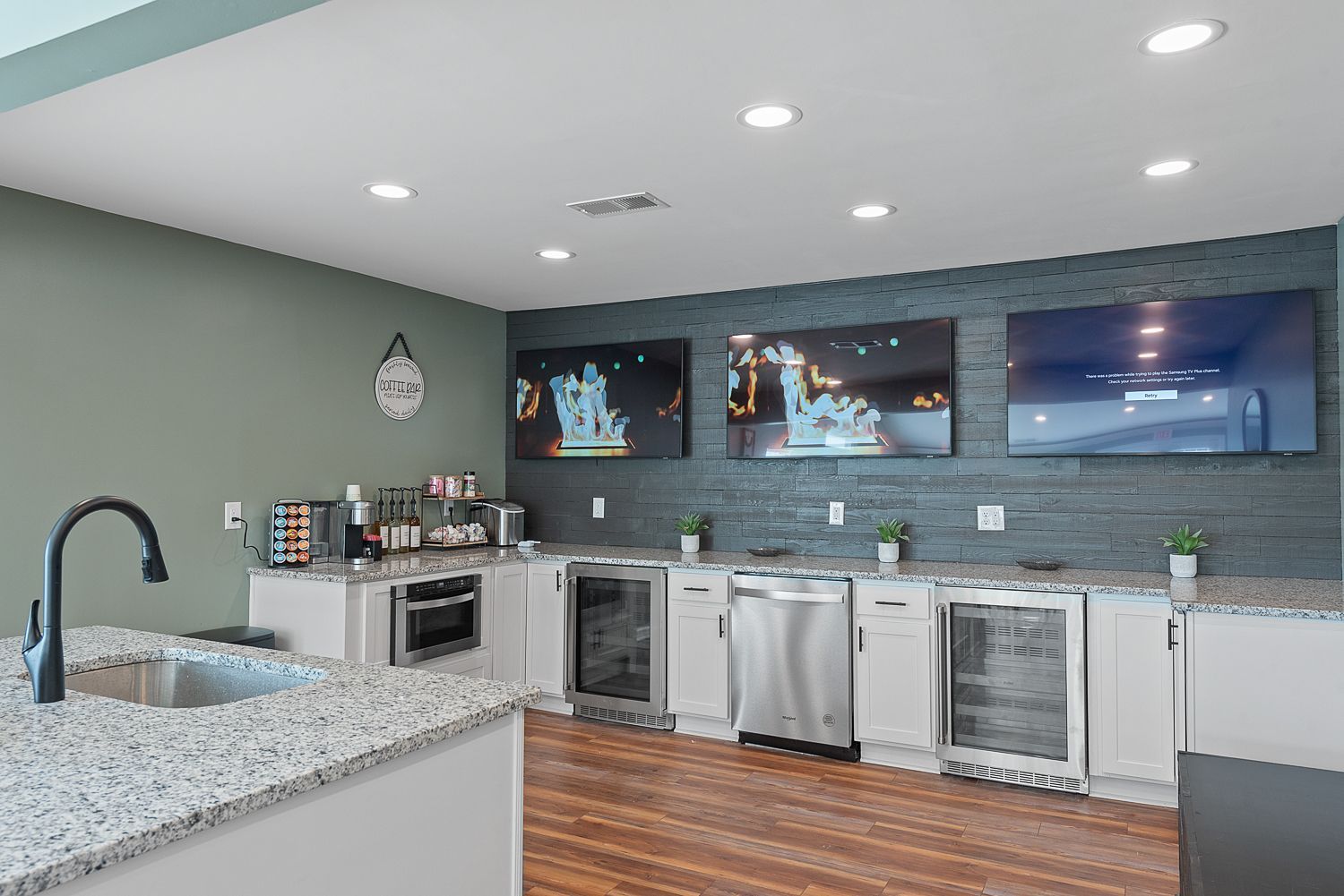 Kitchen with three TVs on a dark blue tiled wall, white cabinets, and granite countertops.