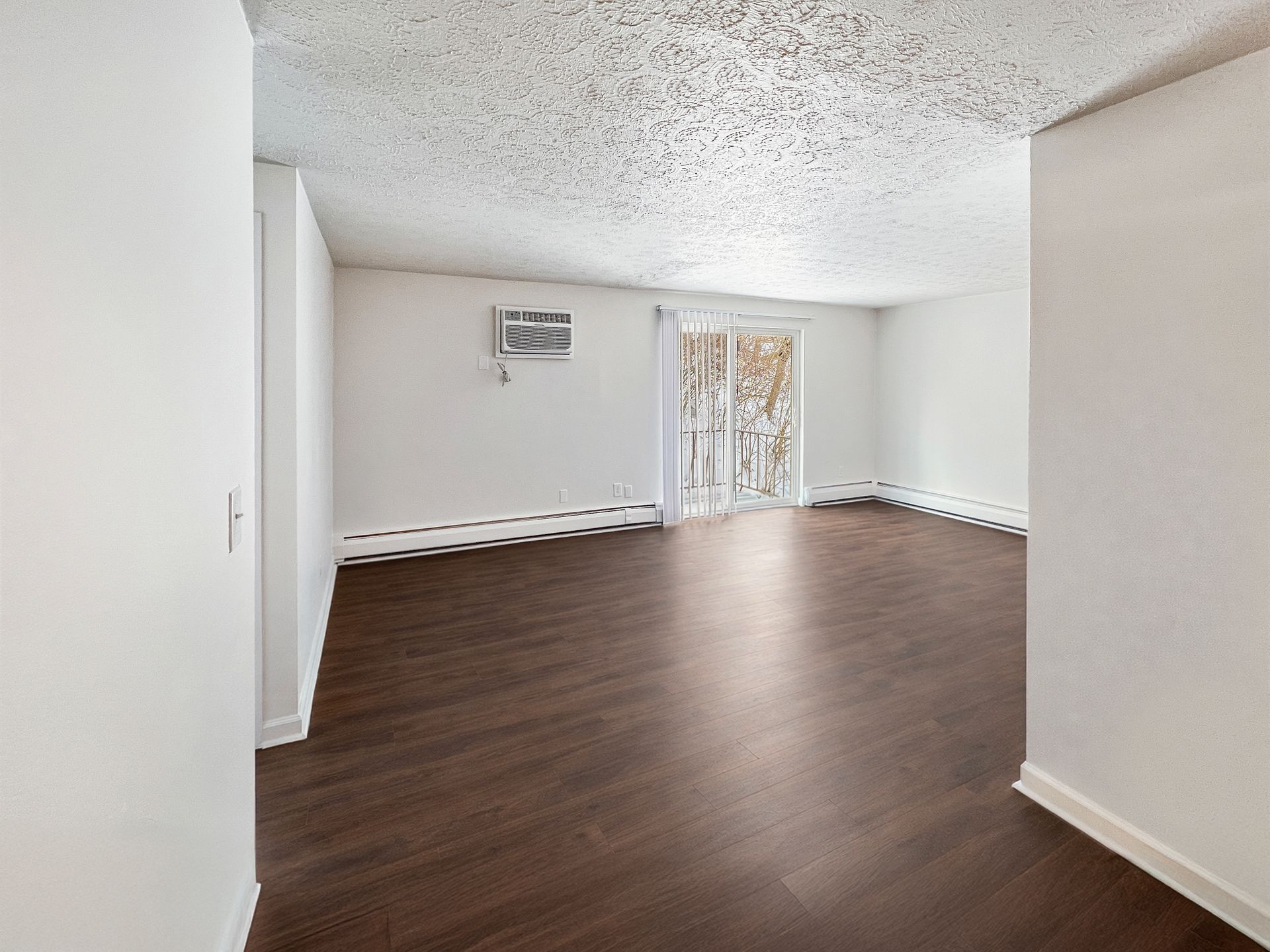 Empty room with wood-look floor, sliding glass door, white walls, and air conditioner.